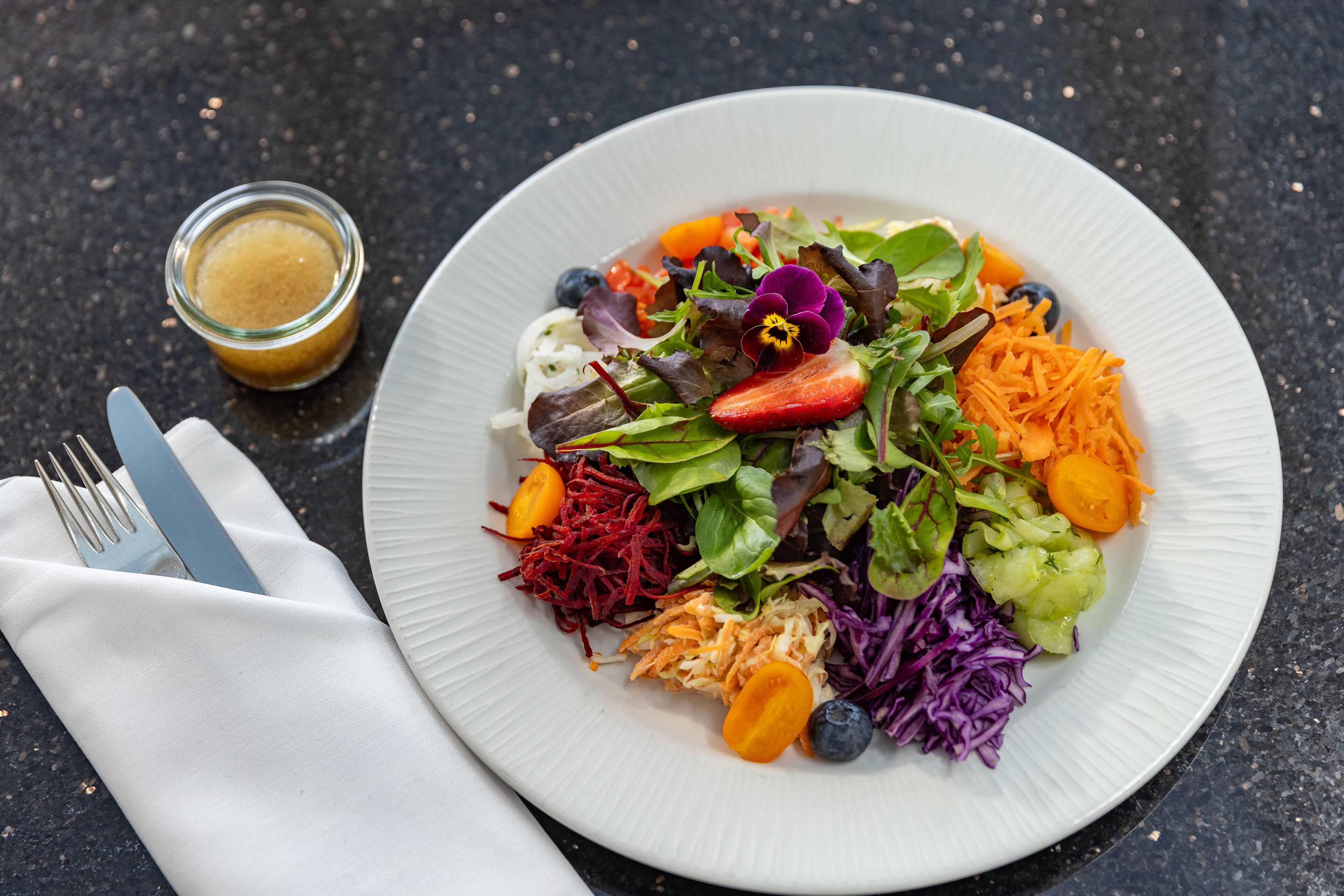 Une assiette de salade colorée, composée de différents légumes, accompagnée d’un petit pot de vinaigrette.