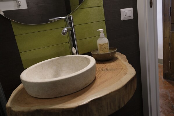 A bathroom with a stone sink, a wooden vanity, and a green wall.