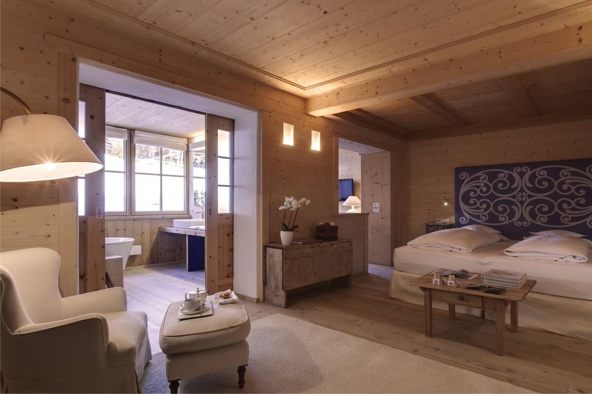 A cozy wooden cabin room with a bed, a chair, a small table, and a window.