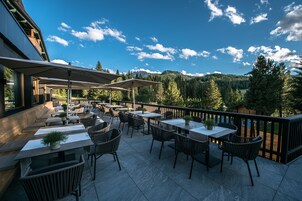 Patio esterno con tavoli e sedie, affacciato su una zona boschiva e montagne.