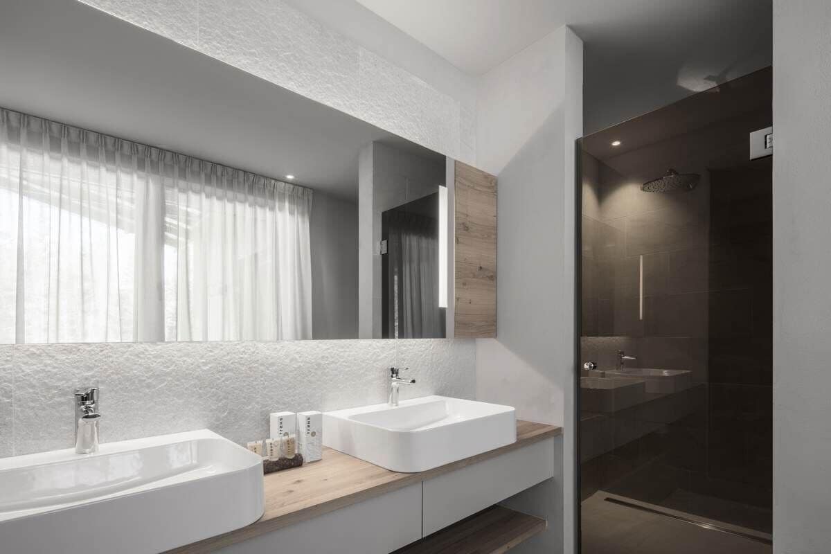 Un baño moderno con dos lavamanos, un espejo grande y una ducha con mampara de vidrio.