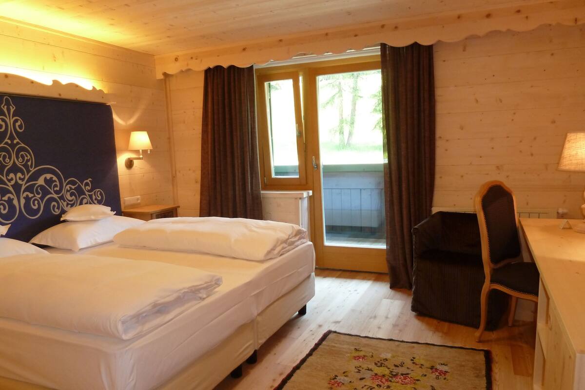 A hotel room with a bed, a desk, a chair, a lamp, and a view of the outdoors.