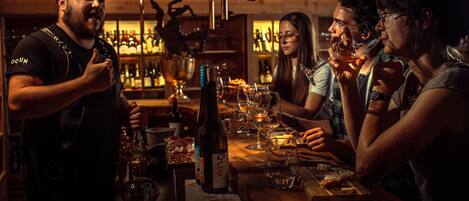 A bar setting with a wooden table, bottles, glasses, and a person standing.