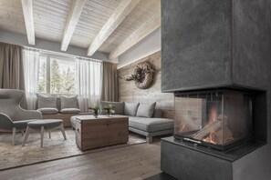 A modern living room with a fireplace, wooden beams, a sofa, and a large window. - Ciasa Salares (Badia)