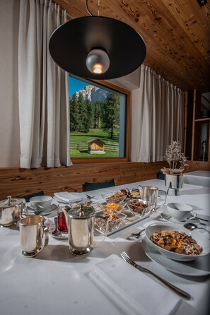 Una mesa de comedor dispuesta con varios platos y cubiertos, un amplio ventanal con vistas a la montaña y un techo de madera.