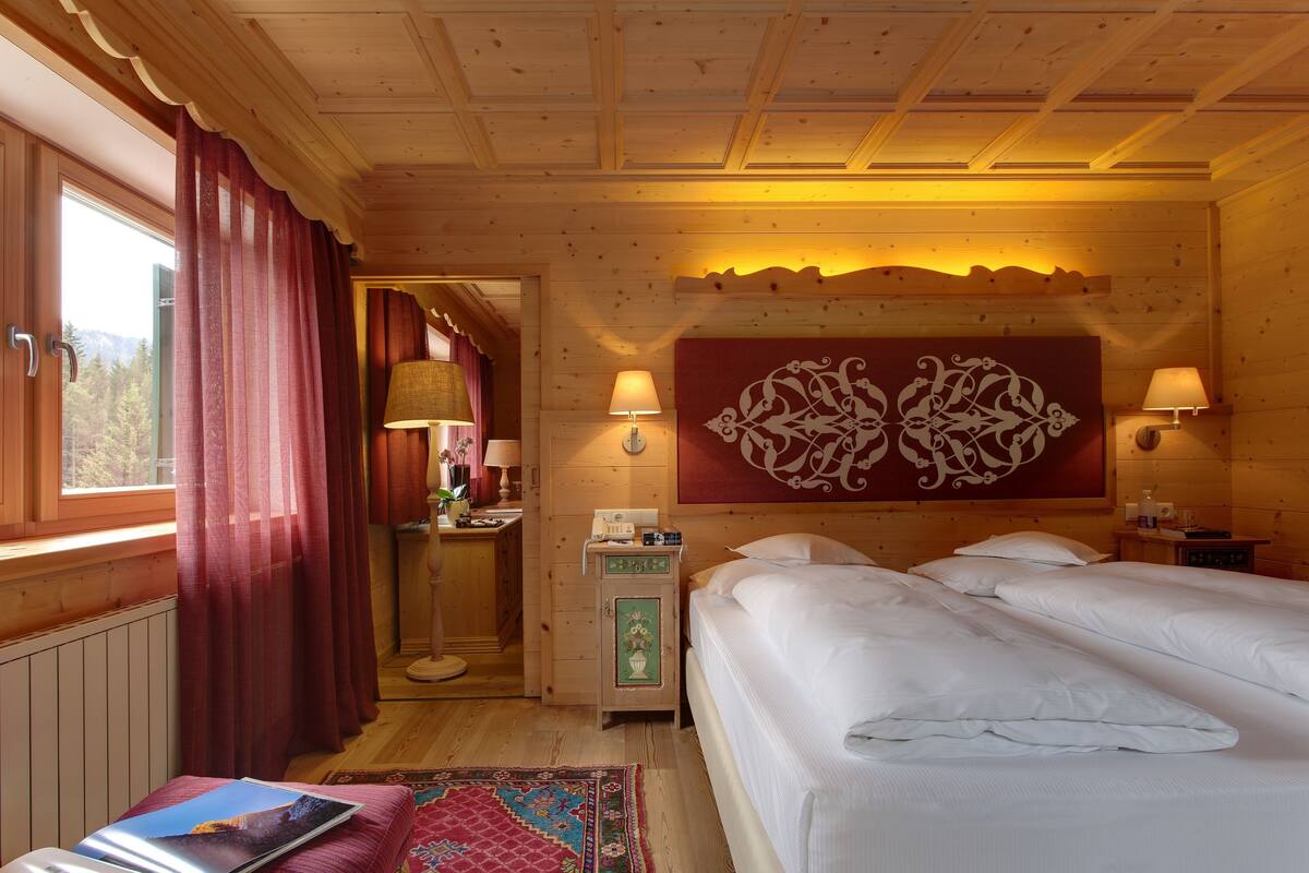 A wooden cabin room with two beds, a nightstand, a lamp, and a view of the outdoors.