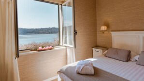 A bedroom with a large window, a bed with striped bedding, a bedside table, and a lamp. - Hotel La Culla del Lago (Castel Gandolfo)