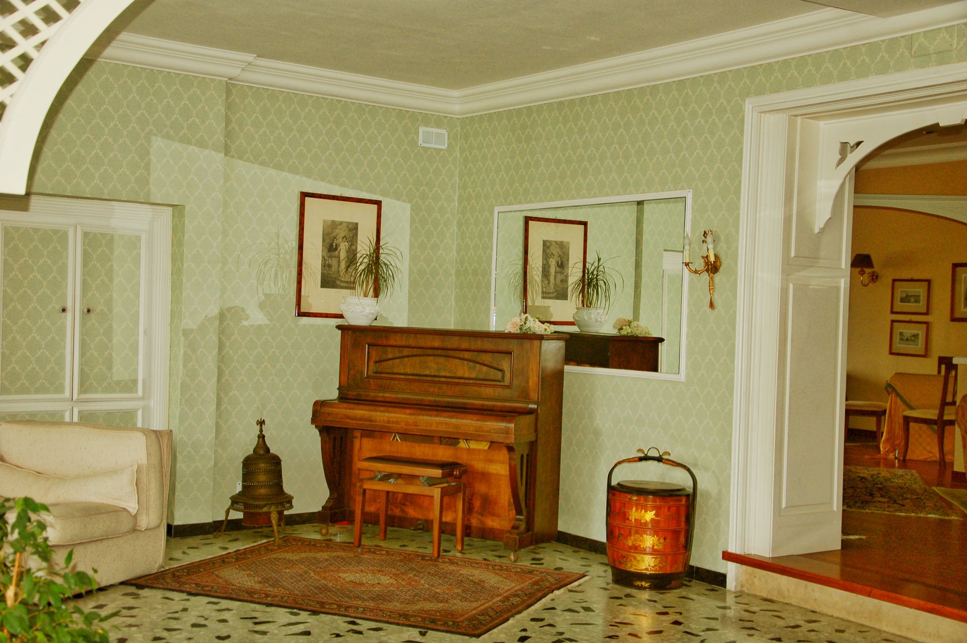 A room with a piano, a sofa, a patterned rug, a decorative lantern, and framed pictures on the walls.