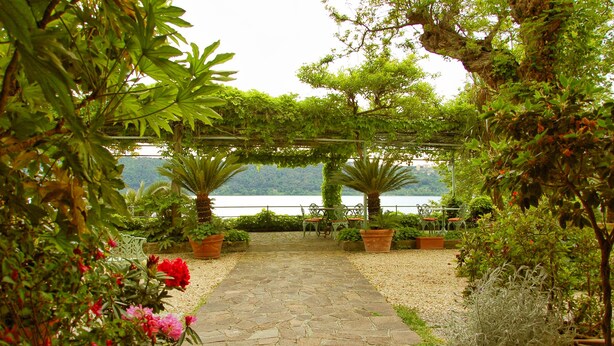 A stone pathway leading to a seating area with chairs and potted plants, overlooking a lake. - Hotel La Culla del Lago (Castel Gandolfo)