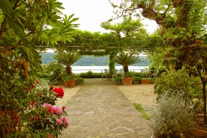 A stone pathway leading to a seating area with chairs and potted plants, overlooking a lake. - Hotel La Culla del Lago (Castel Gandolfo)