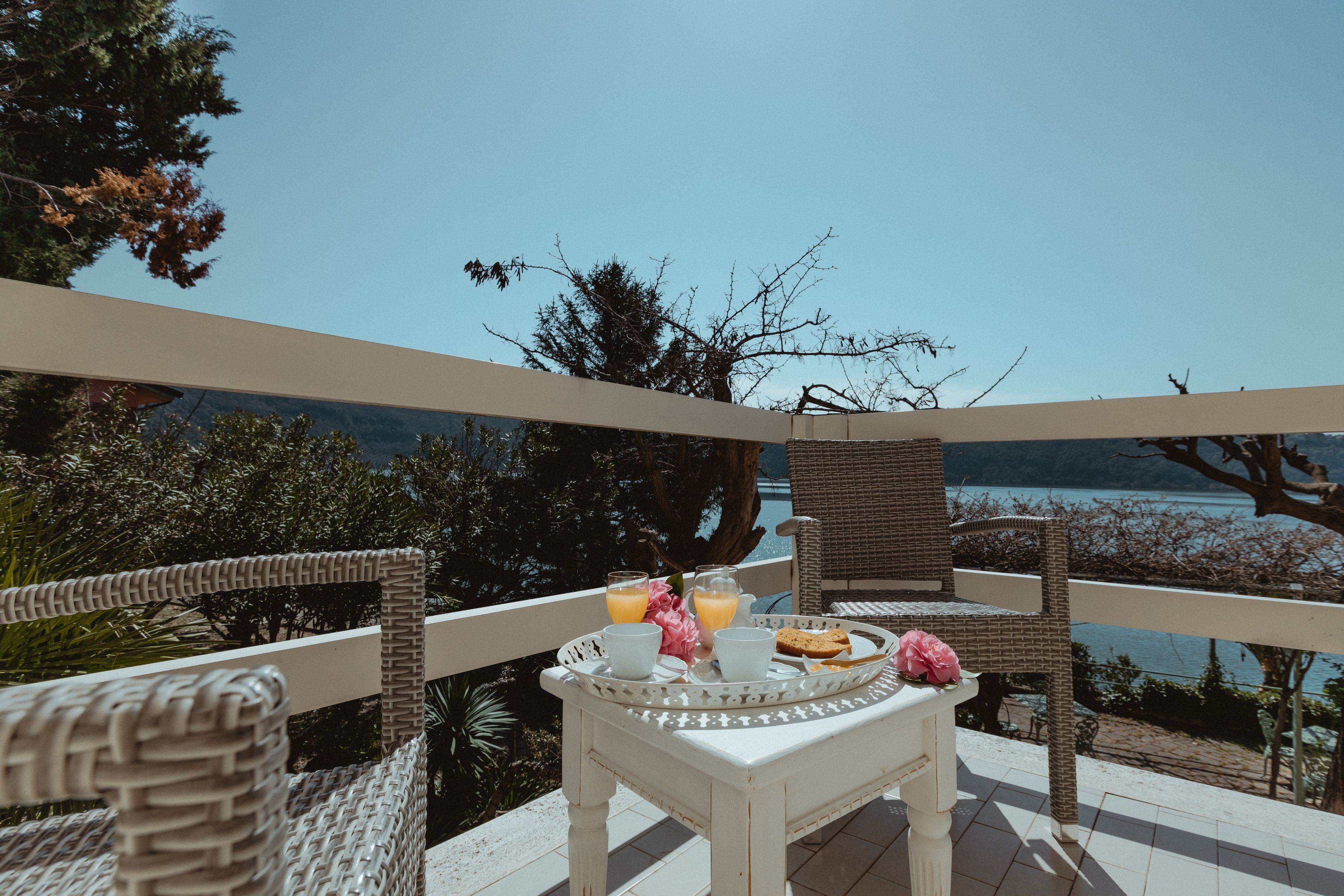 A balcony with wicker furniture, a table with a tray of food and drinks, and a view of a lake.