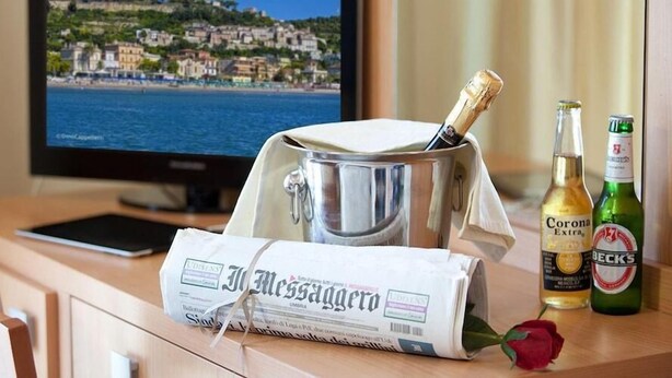 A hotel room with a wooden desk, a newspaper, a champagne bottle, and a bottle of Corona Extra. - Ambassador (Tortoreto)