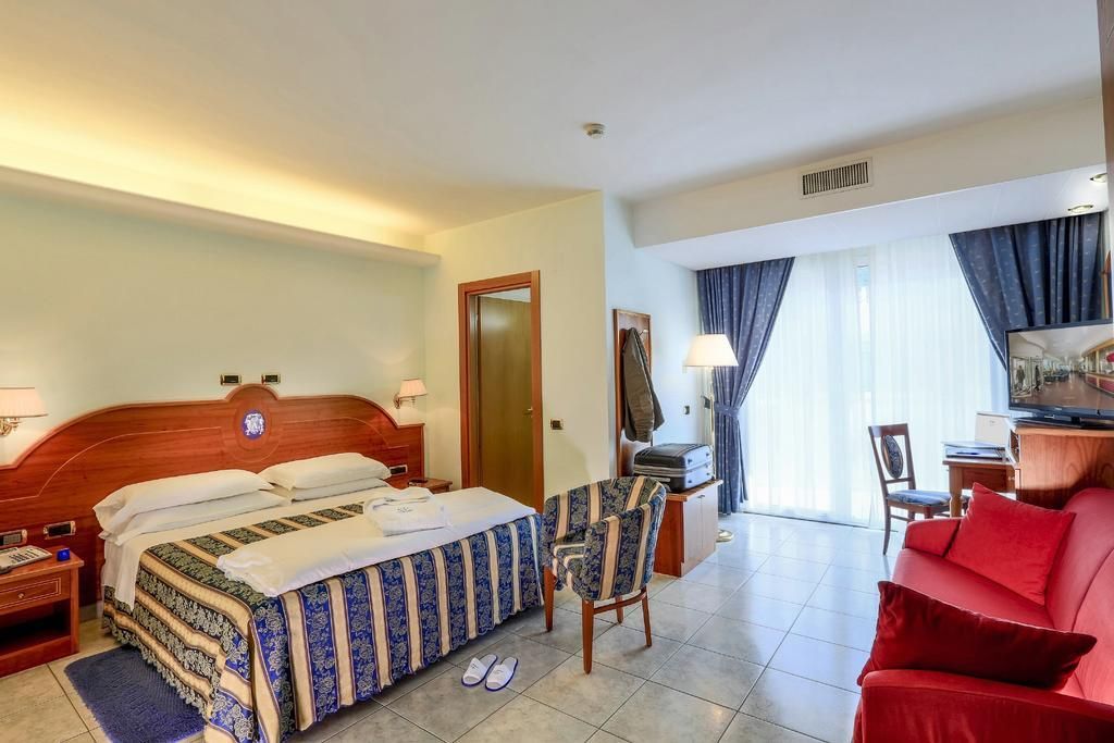 Une chambre d’hôtel avec un lit, un bureau, un canapé rouge, une chaise et un téléviseur.