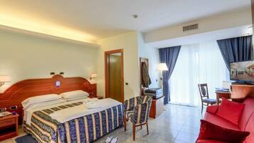 Une chambre d’hôtel avec un lit, un bureau, un canapé rouge, une chaise et un téléviseur.