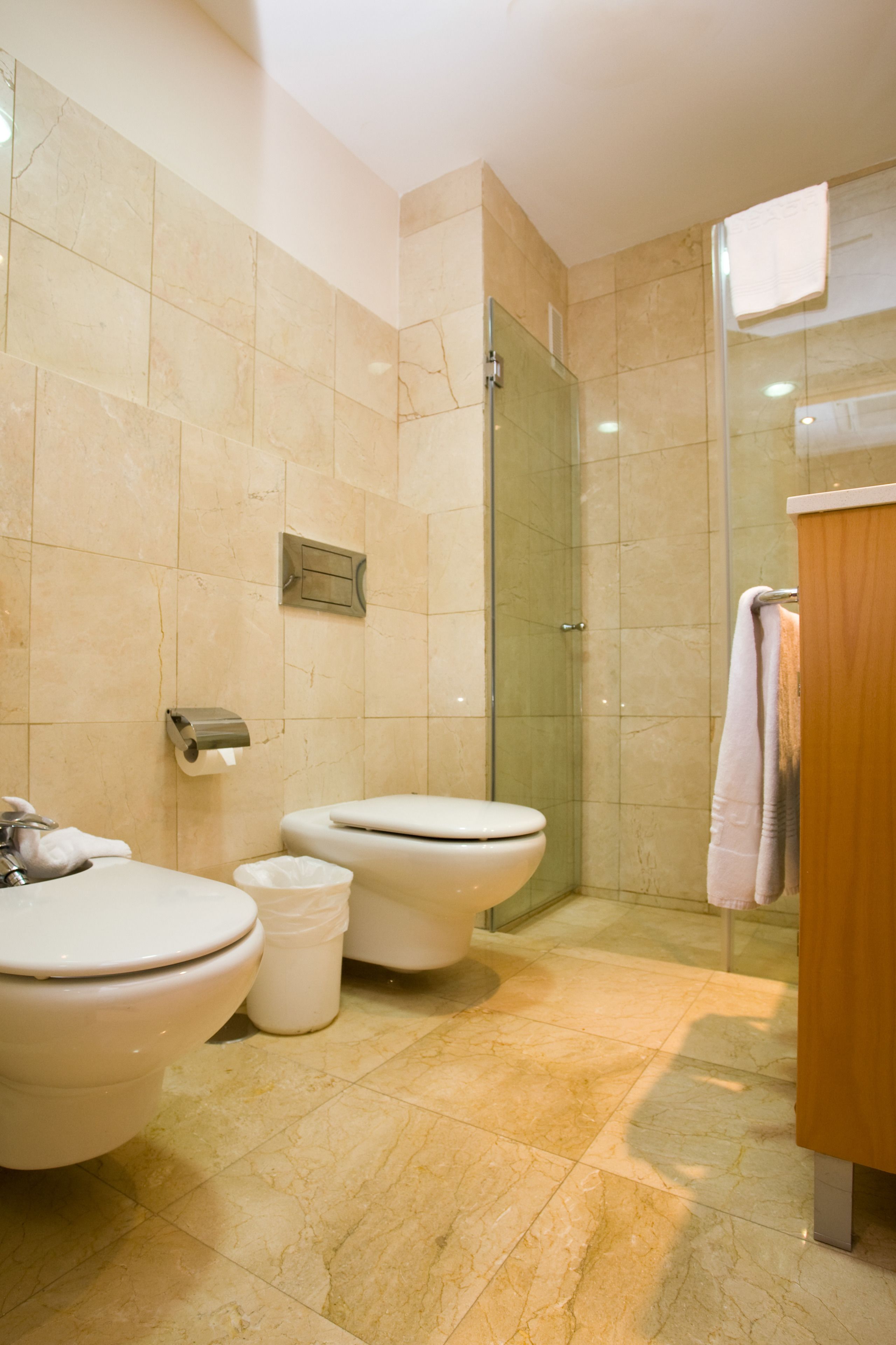 A modern bathroom with two toilets, a sink, a glass shower enclosure, and a wooden vanity.
