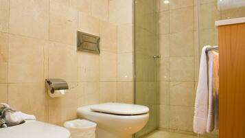 A modern bathroom with two toilets, a sink, a glass shower enclosure, and a wooden vanity.