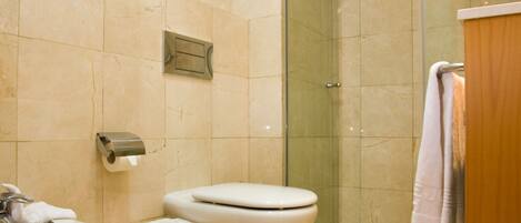 A modern bathroom with two toilets, a sink, a glass shower enclosure, and a wooden vanity.