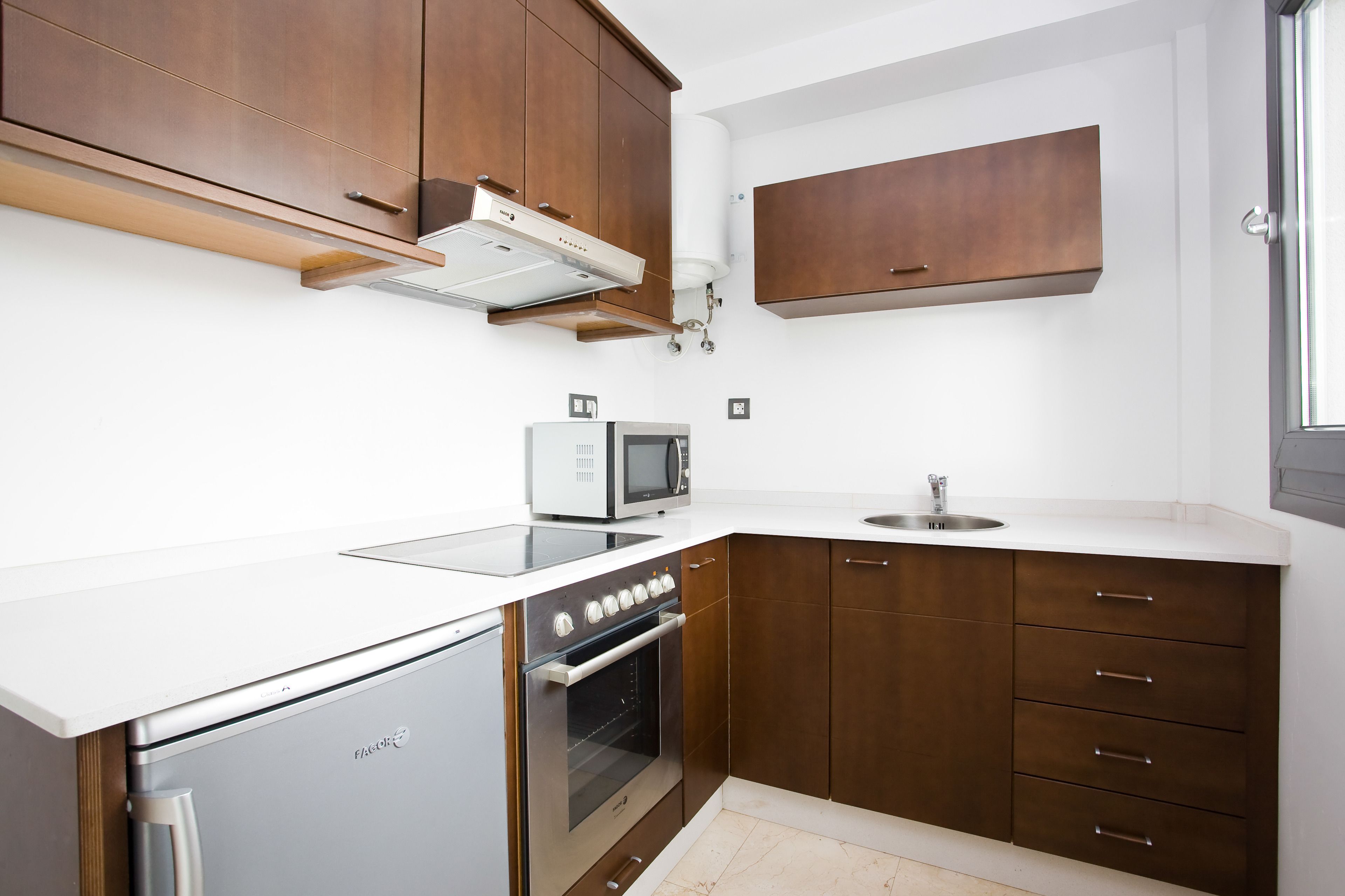 A modern kitchen with wooden cabinets, a white countertop, a built-in microwave, a stainless steel oven, and a dishwasher.