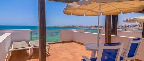 A terrace with a view of the sea, a table, chairs, and an umbrella.