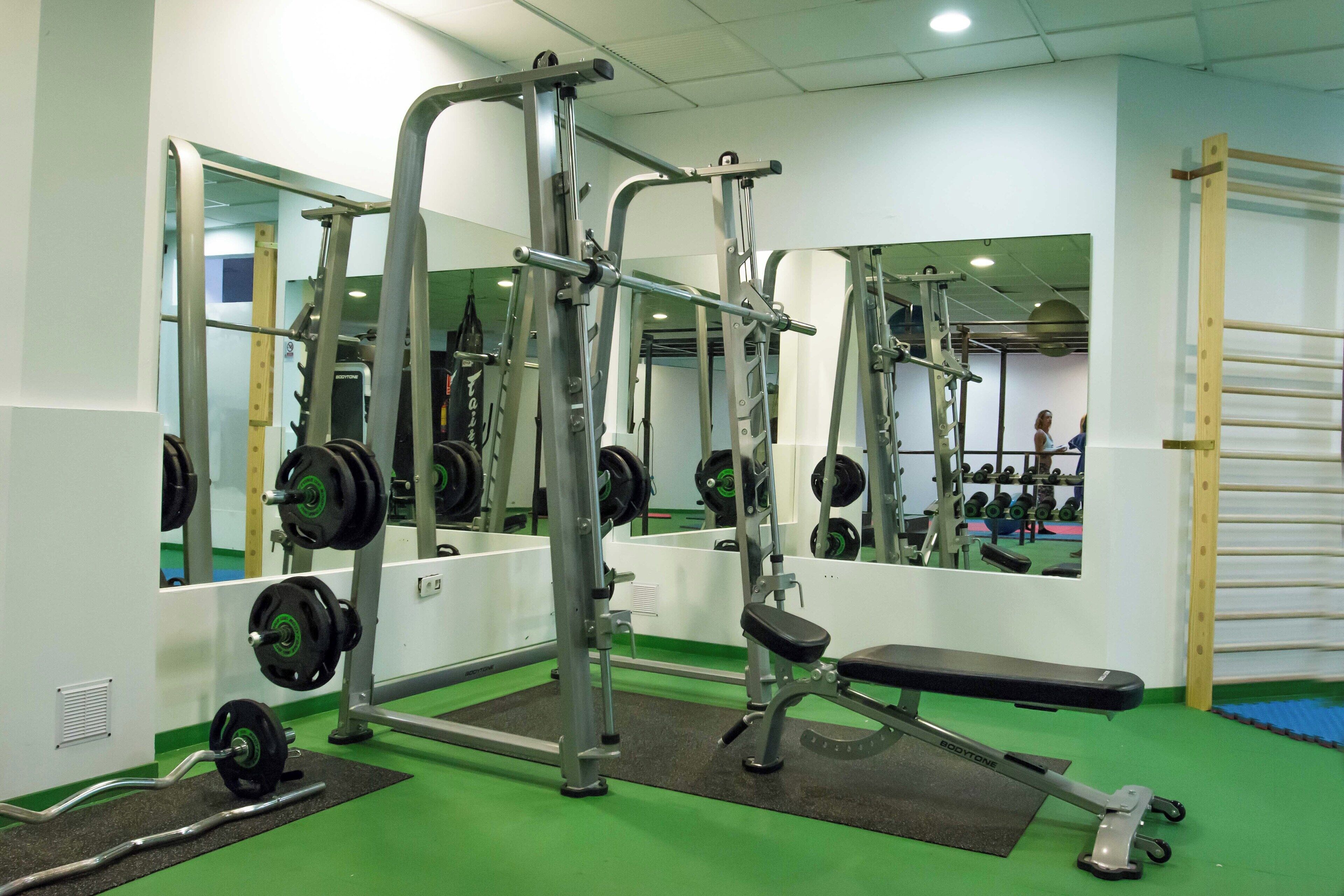 A gym with weightlifting equipment, mirrors, and a bench.