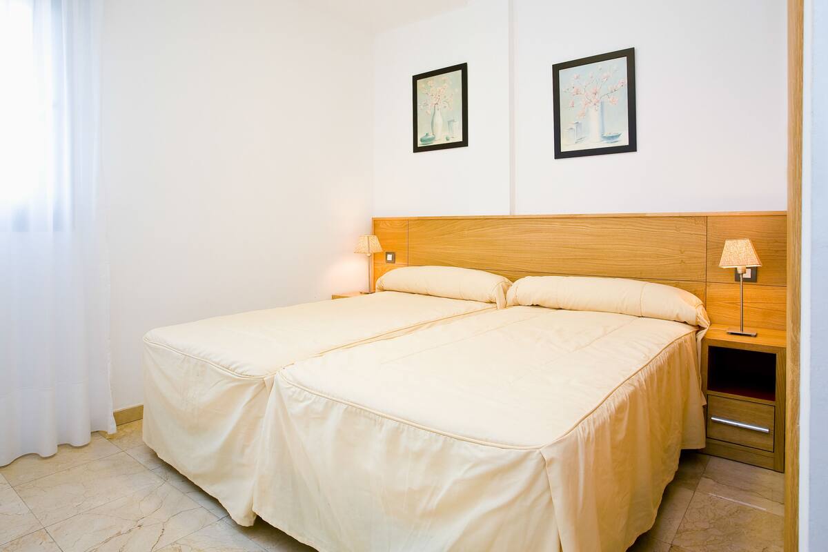 Un lit double avec une tête de lit en bois, deux tables de chevet avec des lampes et deux tableaux encadrés accrochés au mur.