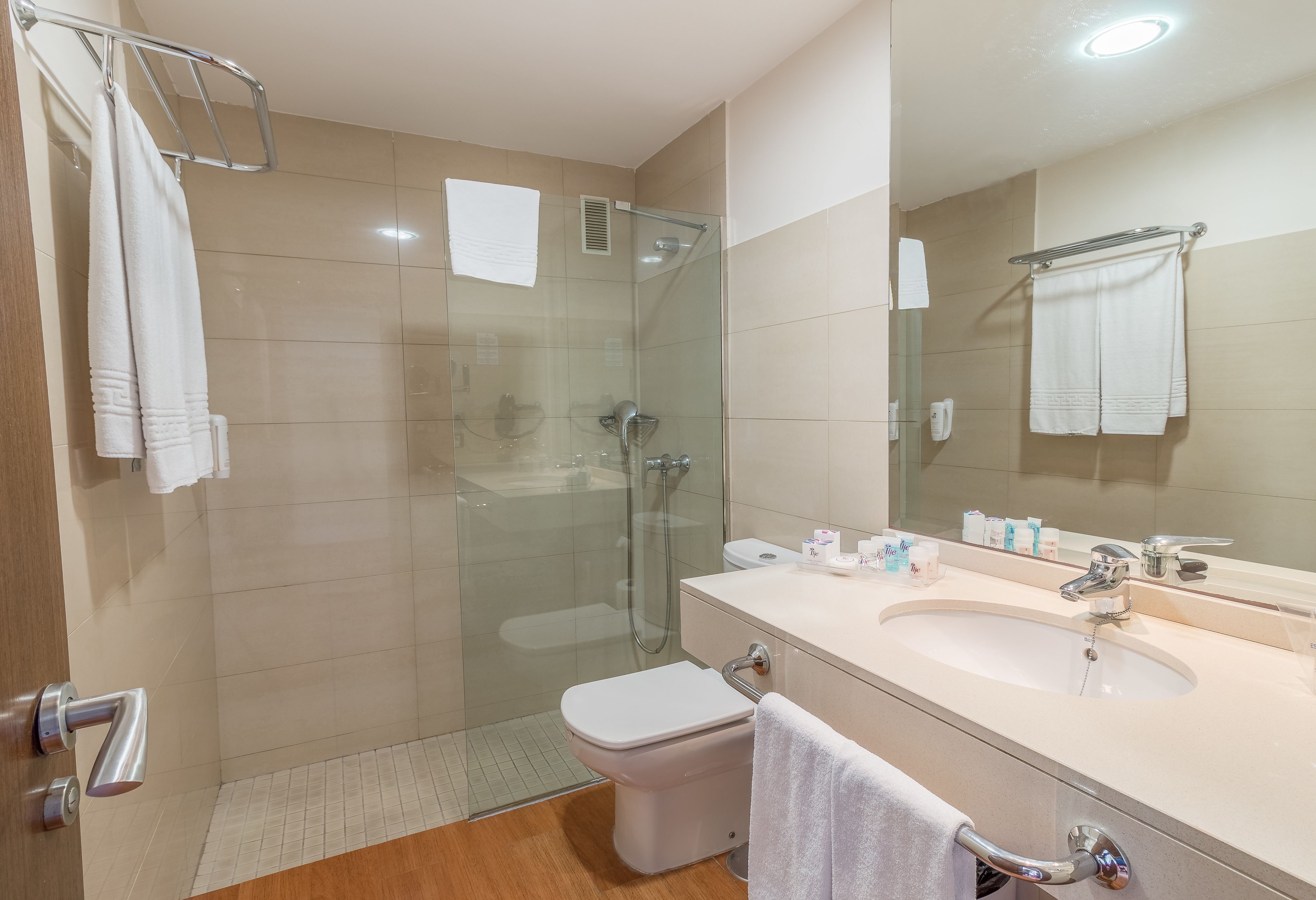 A modern bathroom with a glass-enclosed shower, a white toilet, a sink with a mirror, and a towel rack.