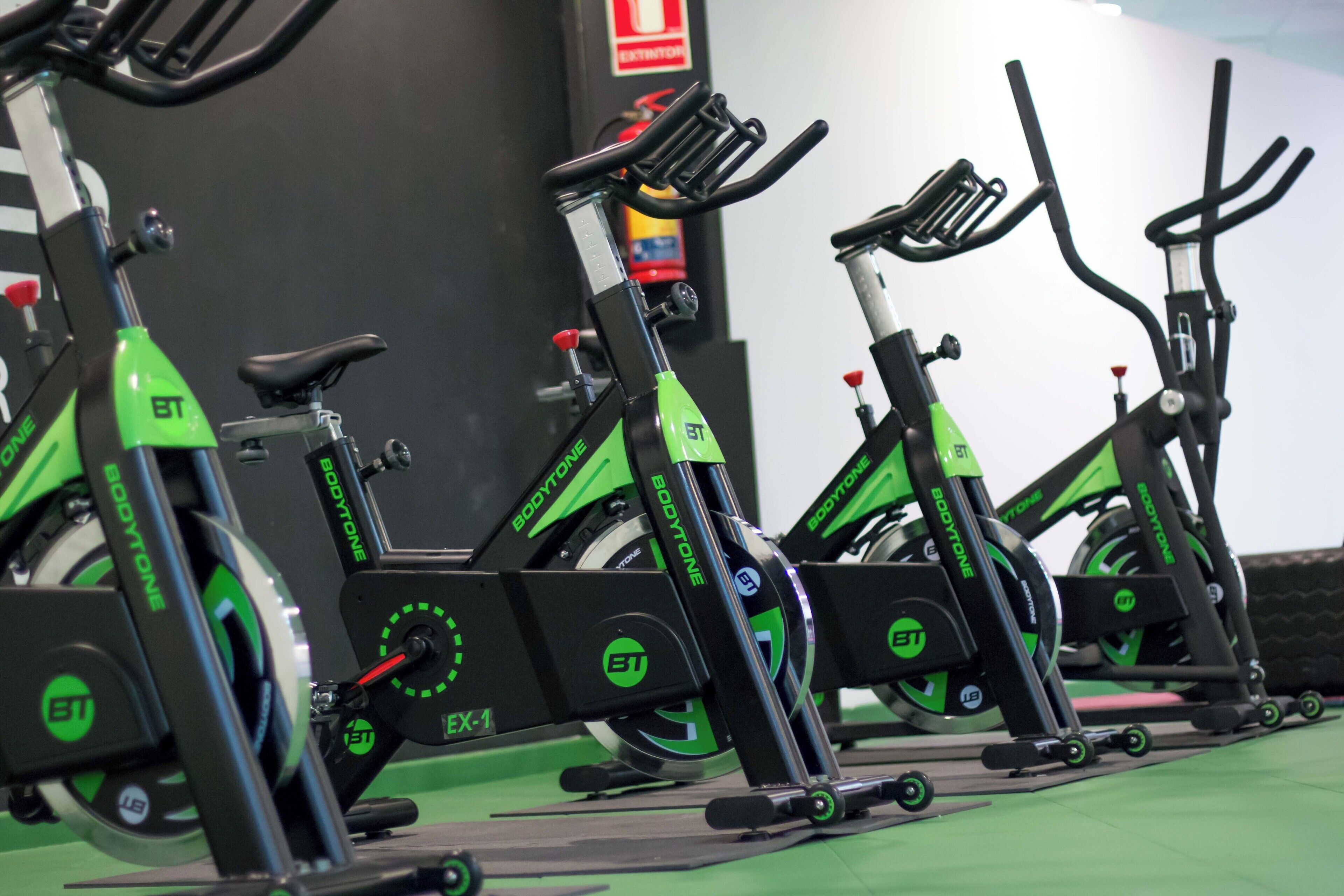 Une rangée de vélos d’appartement, de couleur verte et noire, portant les logos « BT » et « BODYTONE », disposés dans une salle de sport.