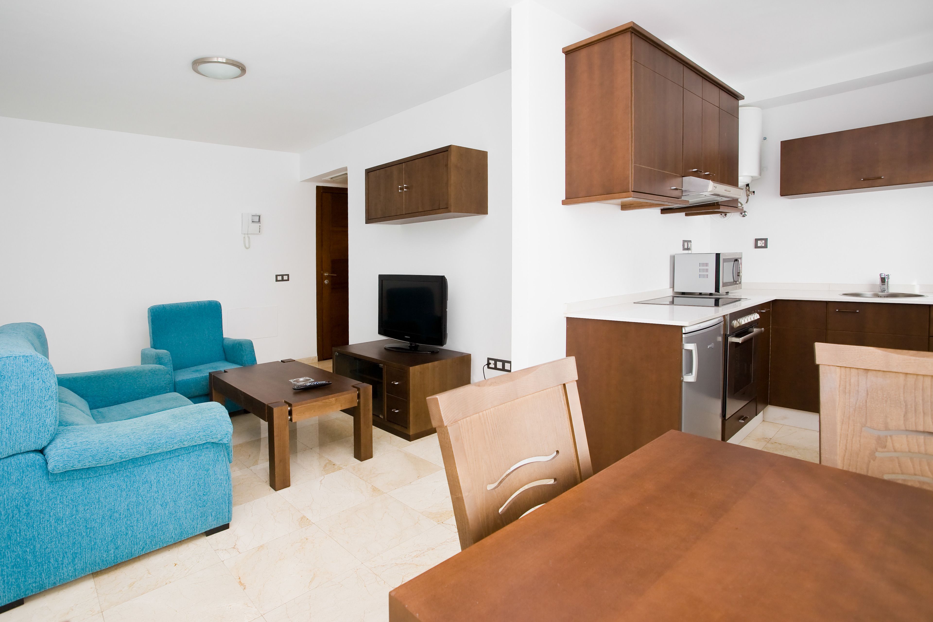 A compact living space with a sofa, TV, wooden dining table, and kitchenette.