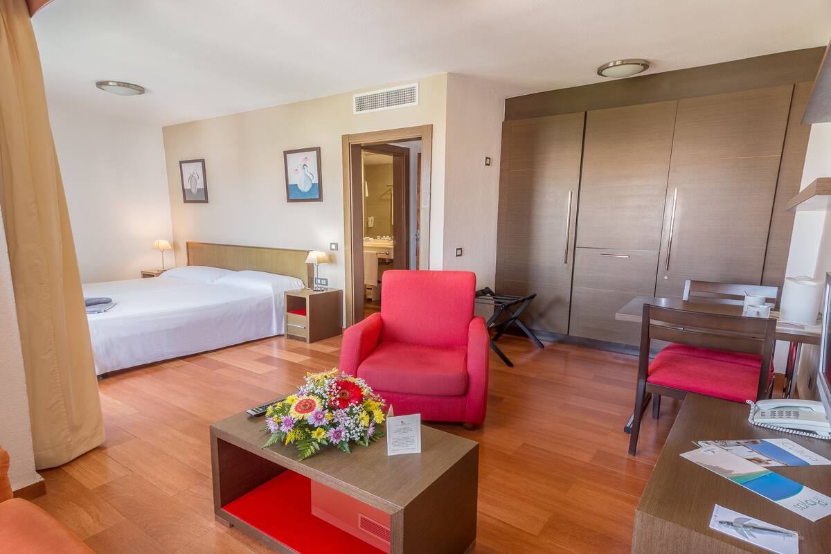 Une chambre d’hôtel avec un lit, un bureau, une chaise et une petite table agrémentée d’un arrangement floral.