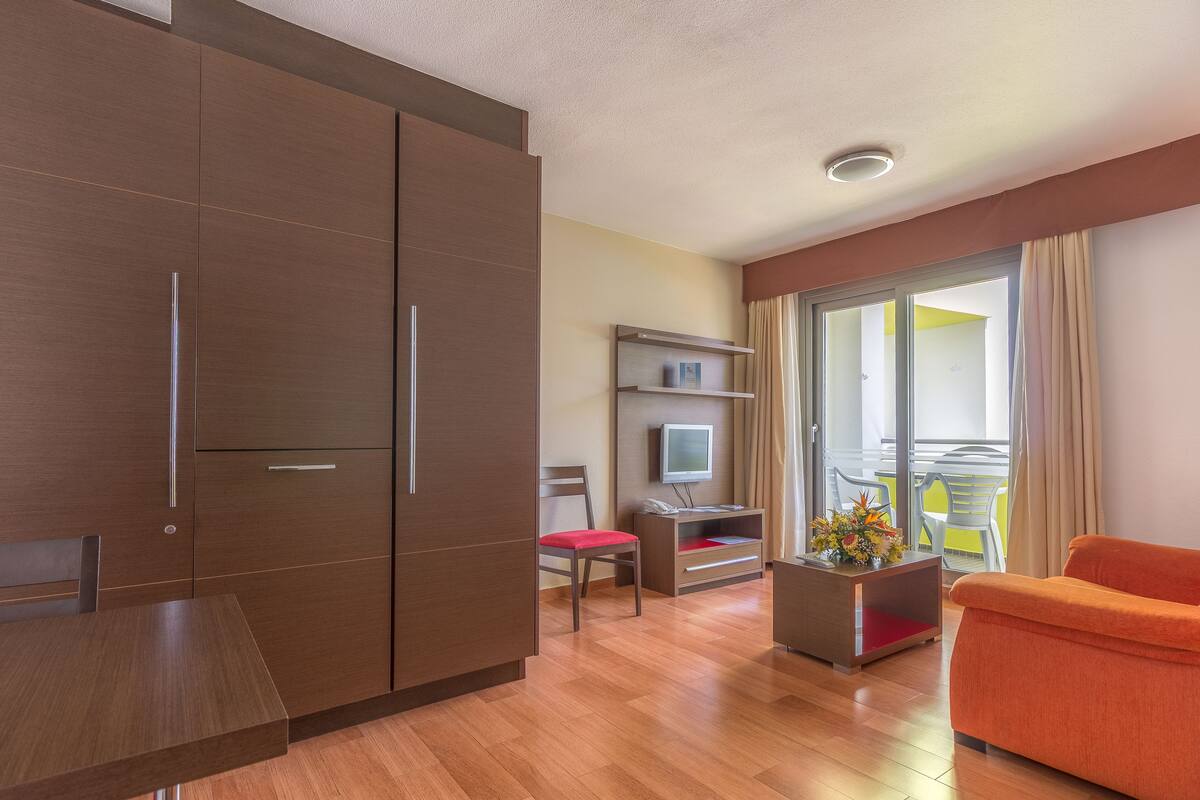 Une chambre d’hôtel moderne avec une armoire en bois, une table à manger, un canapé, une télévision et un balcon avec vue.