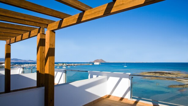 Een houten balkon met uitzicht op zee, boten en een berg in de verte.