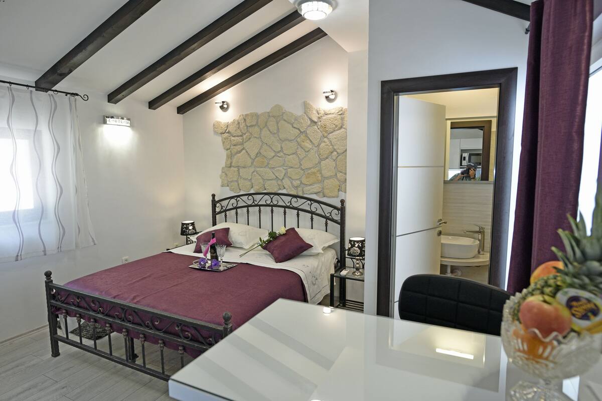 Ein Schlafzimmer mit Bett, Nachttischen, einem Spiegel und Blick ins Badezimmer.