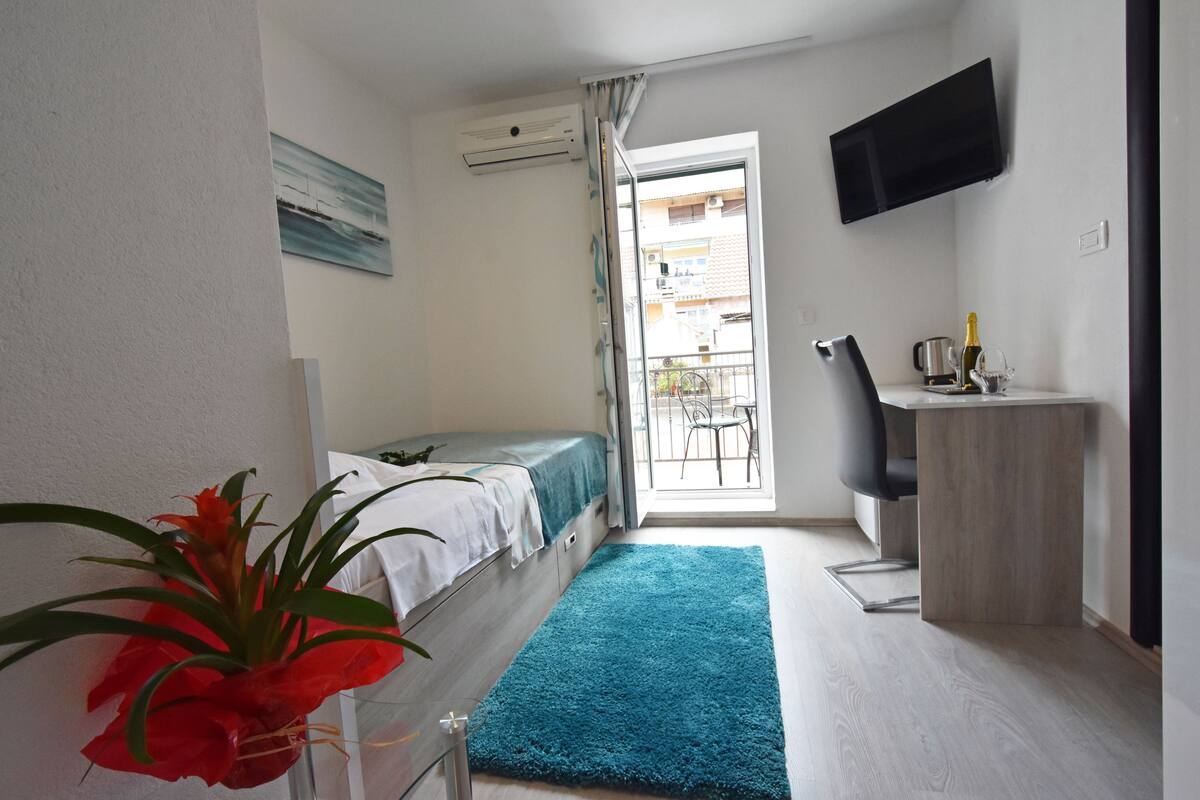 Ein Schlafzimmer mit Bett, Schreibtisch, Stuhl, Fernseher und Balkon.