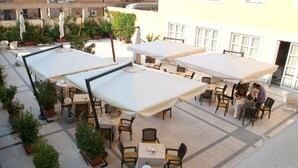 An outdoor patio area with tables and chairs, surrounded by potted plants and umbrellas. - Hotel San Domenico al Piano (Matera)