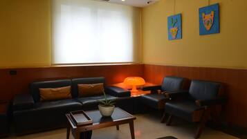 A modern living room with a black leather sofa, a wooden coffee table, and a blue armchair. There is a potted plant on the coffee table and a lamp on the sofa.