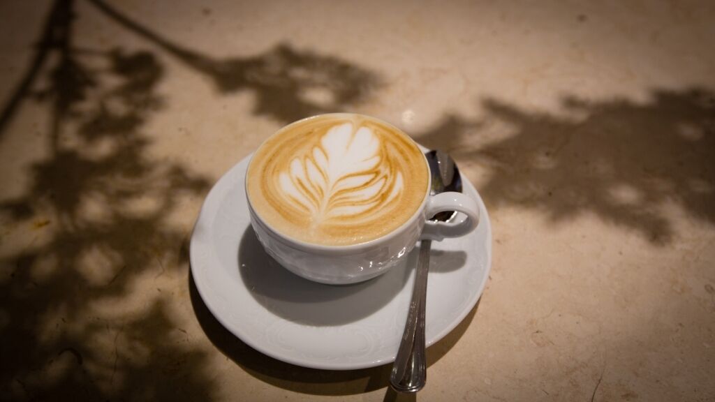 Une tasse de café ornée d’un motif en latte art, posée sur une soucoupe, elle-même placée sur une table.