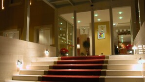 A staircase with red carpeted steps leading to a reception area with glass doors and a reception desk. - Hotel San Domenico al Piano (Matera)