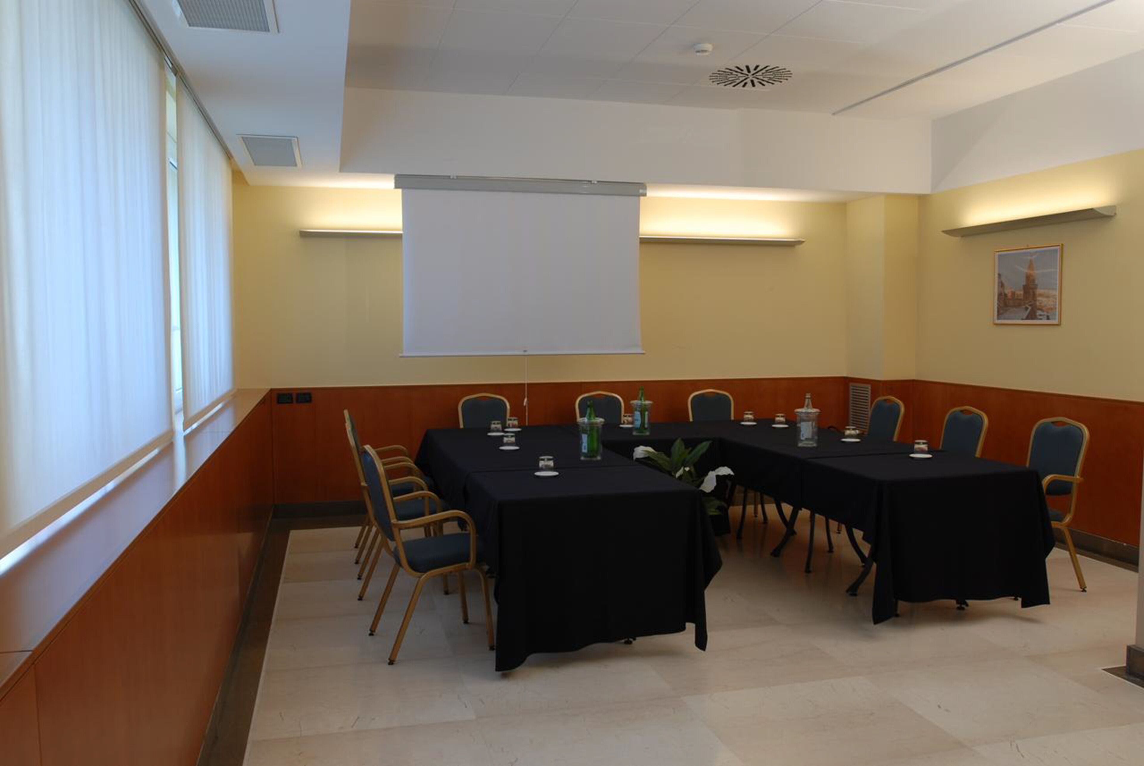 A conference room with a long table, chairs, a projector screen, and a framed picture on the wall.