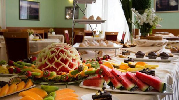 A buffet table with various fruits, a watermelon carved into a decorative shape, and a cake on a plate. - Hotel San Domenico al Piano (Matera)