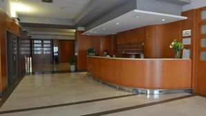 A reception area with a curved wooden counter, potted plants, and a clean tiled floor. - Hotel San Domenico al Piano (Matera)