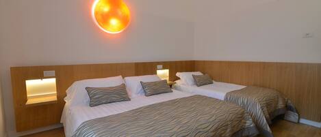 A hotel room with two beds, a wooden headboard, and wall-mounted lamps.
