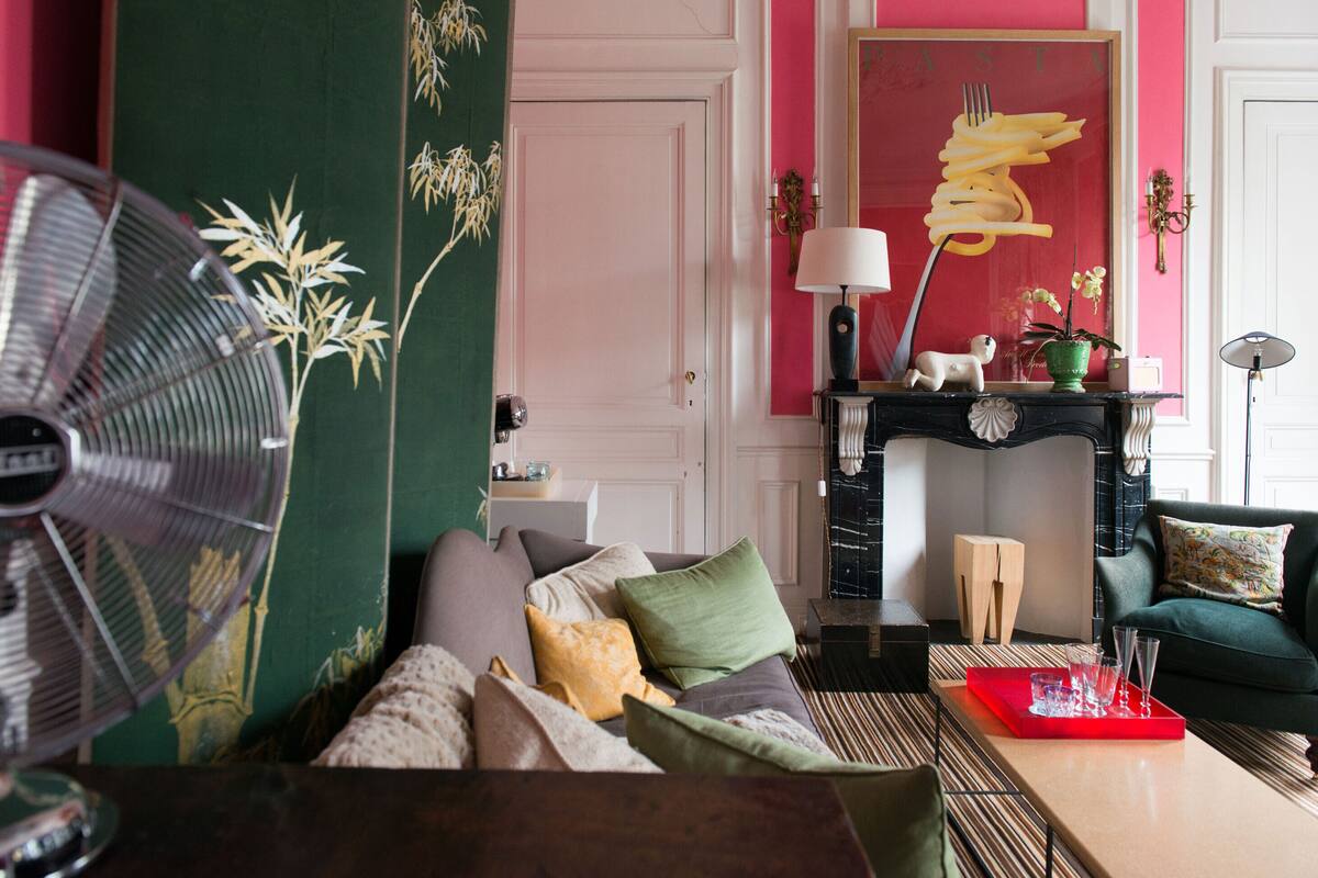 A living room with a sofa, a fan, a fireplace, and a red wall.