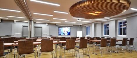 A conference room with rows of tables and chairs, a large screen, and a modern ceiling design.