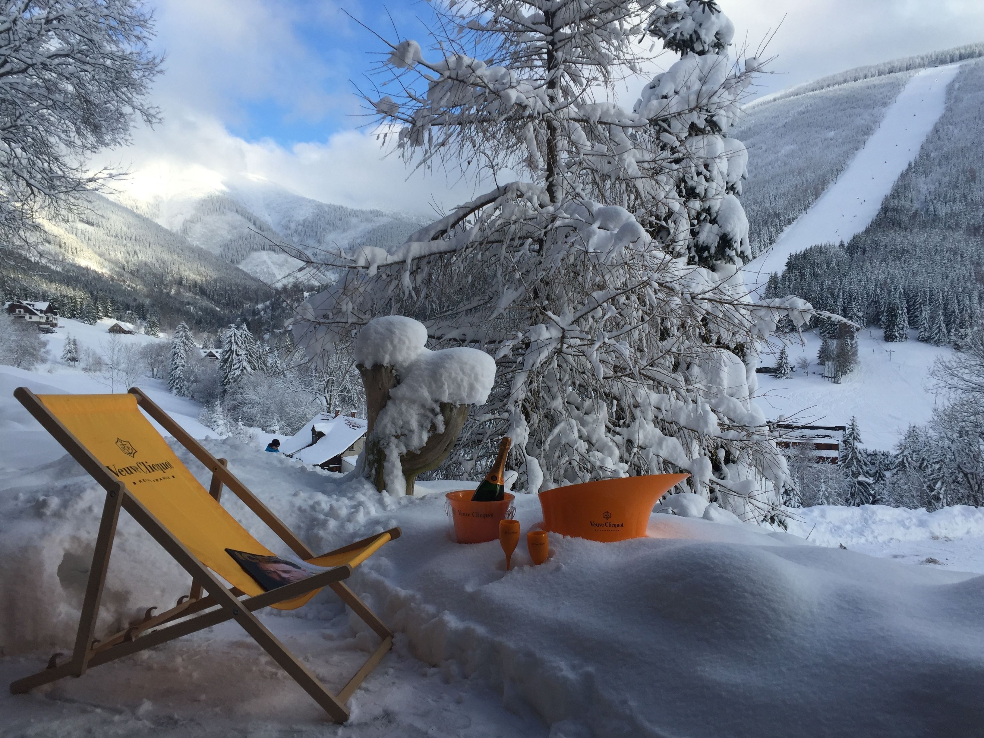 A snow-covered chair and bucket in a mountainous area with a view of houses and trees.