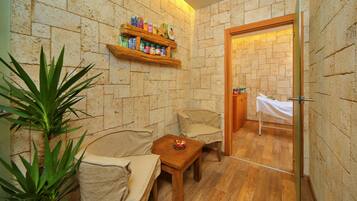 A small, cozy room with a wooden floor, a beige sofa, a wooden table, and a shelf with toiletries.