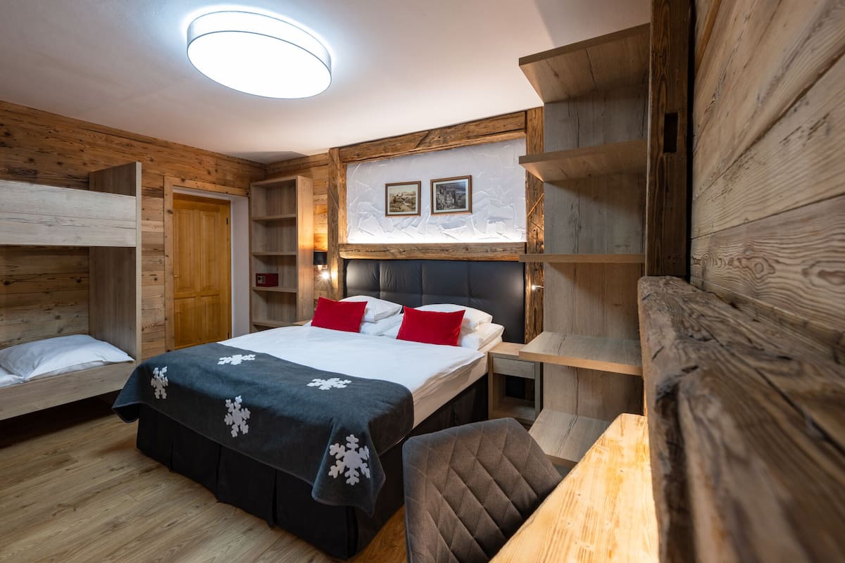 Una habitación acogedora con una cama, una silla, paredes de madera y una estantería con fotografías.