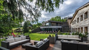 Un área lounge exterior moderna con mobiliario de mimbre, una terraza de madera y vistas a un edificio con balcón.