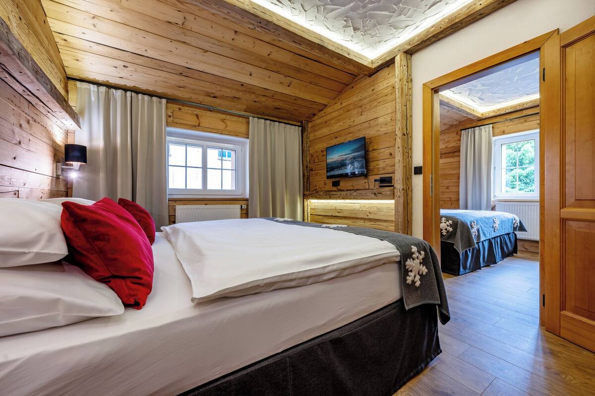 Una habitación con paneles de madera, una cama, un televisor montado en la pared y vistas al exterior a través de una ventana.