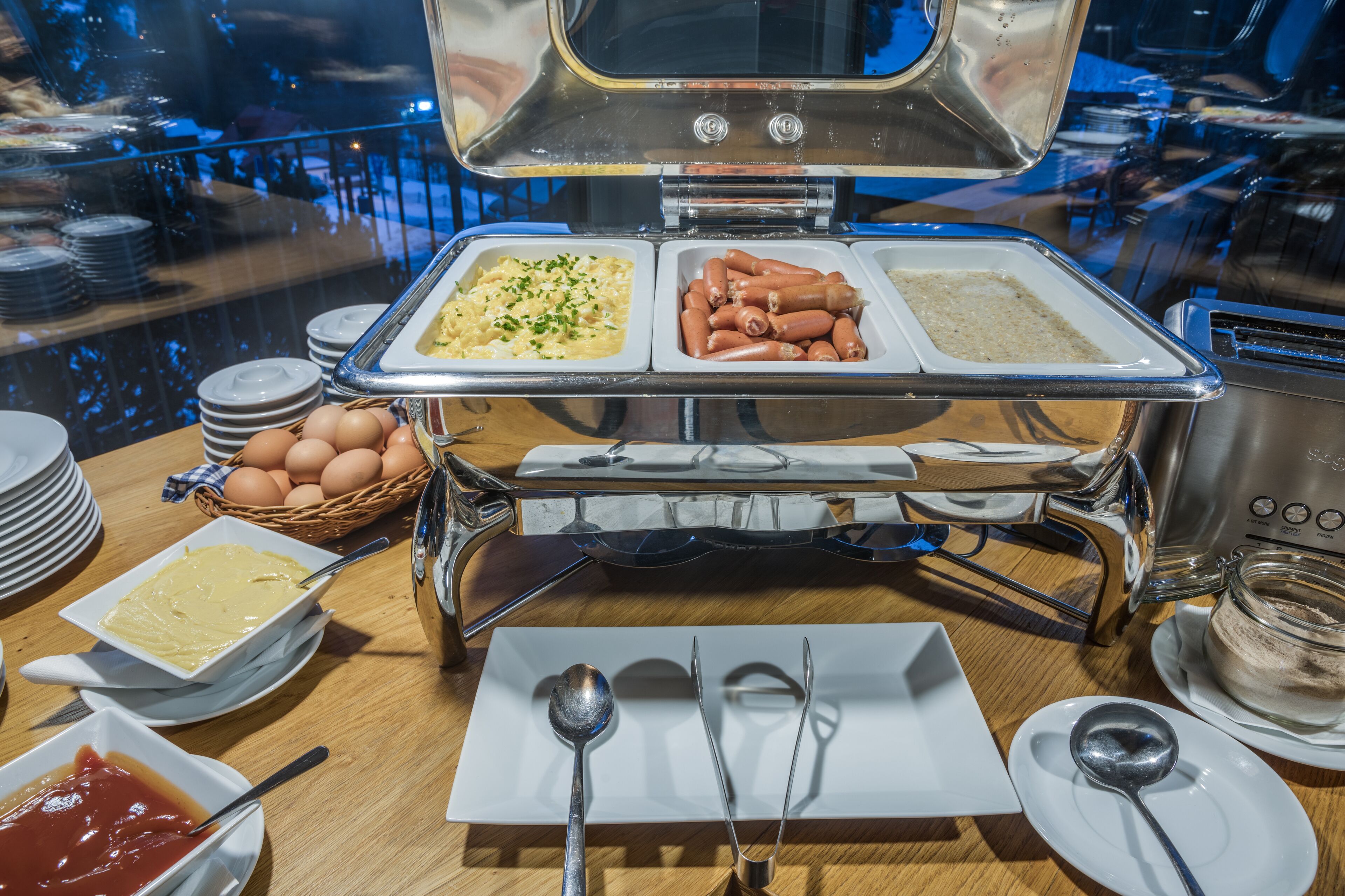 A buffet setup with various food items, including macaroni, sausages, and eggs.