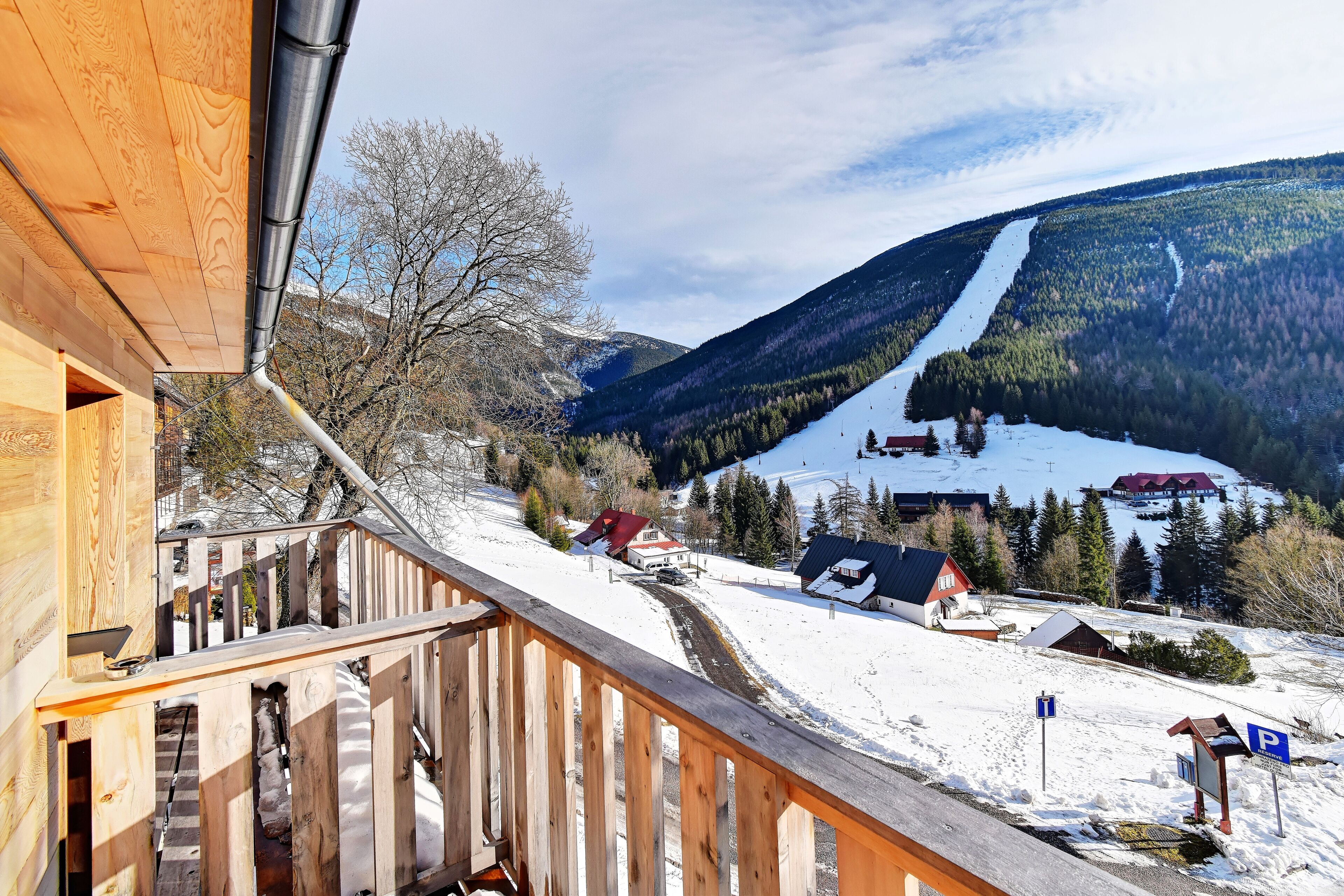 A wooden balcony with a view of a snowy mountain landscape, including a ski lift and buildings.